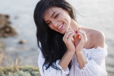 Sahildeki mutlu kadın. Deniz arka plan üzerinde yakın çekim güzel bir kız portresi. Sahilde bahar portresi. Genç güzel kız. Genç gülümseyen kadın açık havada portre. Okyanusun kayalık kıyısında güzel genç kadın