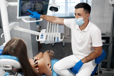 Diş sağlığı kliniği. Resepsiyon, hastanın muayenesi. Diş bakımı. Genç bir kadın diş hekimi tarafından muayene ediliyor. Mutlu hasta ve dişçi konsepti. Diş muayenesinde erkek dişçi kız hastayla konuşuyor. Güzel dişler.