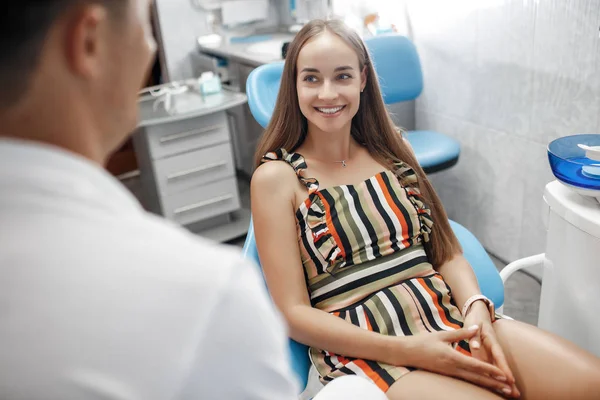 Dental clinic. Reception, examination of the patient. Teeth care. Young woman undergoes a dental examination by a dentist.Happy patient and dentist concept.Male dentist in dental office talking with girl patient.Beautiful teeth