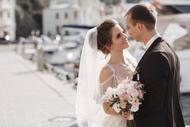 Bir çift aşık, yatların yanındaki iskelede yürüyor. Yazın açık havada aşk yaşayan genç bir çift, arka planda güzel beyaz yatlar ve sakin bir denizde rıhtımda kucaklaşıyorlar. Harika bir çift yeni evli çift, deniz kenarında rıhtımda yürüyor.