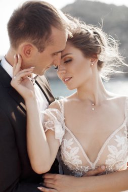 Gelin ve damat, deniz, dağlar ve ada manzarasının arka planında birbirlerine bakıyorlar. Yeni evliler düğün töreninden sonra kalıyorlar. Gelin klasik beyaz bir gelinlik ve uzun bir duvak giyiyor..