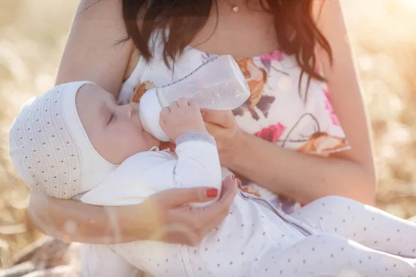Mother feeding her newborn baby boy from bottle outdoors in the field. artifitial milk feedng — Stock Photo, Image