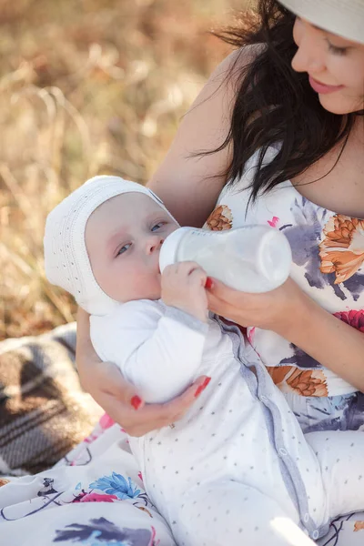 Mãe alimentando seu bebê recém-nascido de mamadeira ao ar livre no campo. alimentação artificial do leite — Fotografia de Stock