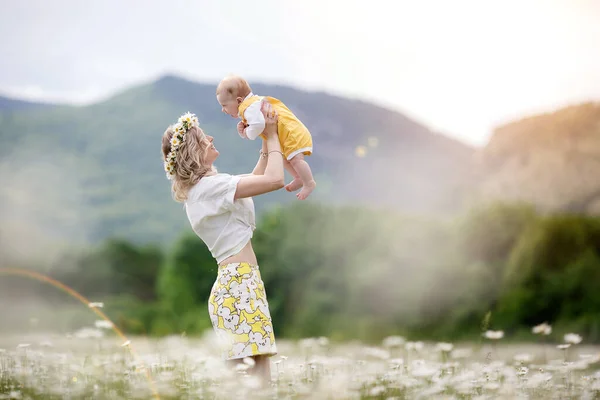 Mujer feliz con el niño pequeño en camomilles. campo blanco floreciente. familia en flores. madre e hijo — Foto de Stock