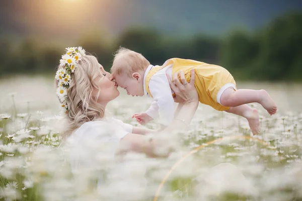Happy woman with little baby boy in camomilles. blooming white field. family in flowers. mother and son — Stock Photo, Image