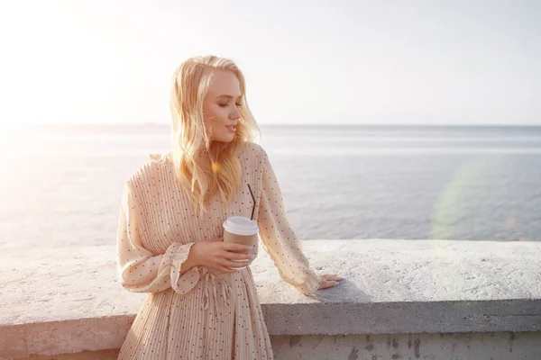 Retrato de uma jovem mulher sorridente com café ao ar livre perto do mar — Fotografia de Stock