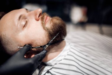 Berber, berber dükkanında bir adamı tıraş ediyor.