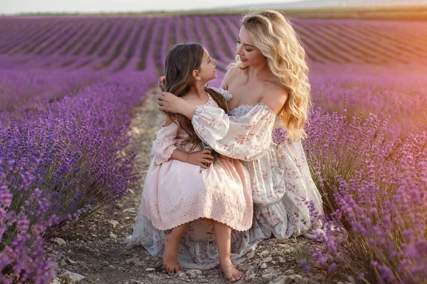 Bonita madre con hija jugando en el campo de lavanda. mujer con niño niña en la luz del atardecer recogida de flores de lavanda —  Fotos de Stock