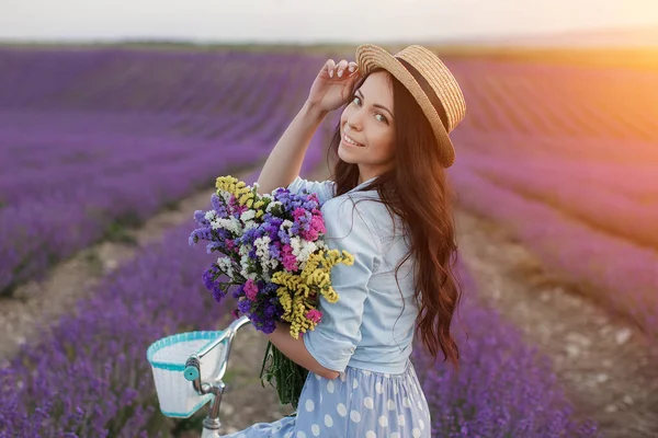 Bonita mujer morena huyendo en el campo de lavanda. mujer en vestido y sombrero de paja divirtiéndose en flores de lavanda —  Fotos de Stock
