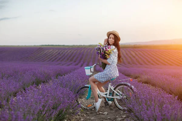 Pěkná brunetka utíká na levandulovém poli. žena v šatech a slamák klobouk baví v květinách levandule — Stock fotografie