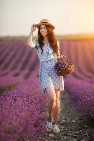 En vacker brunett som springer iväg på lavendelfältet. kvinna i klänning och halm hatt har kul i blommor av lavendel — Stockfoto