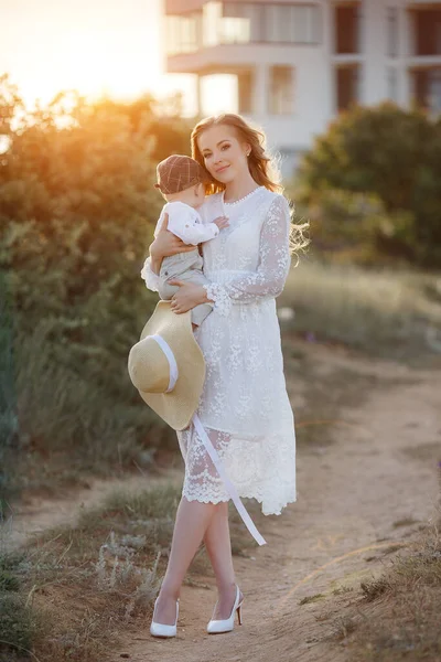 Mooie mooie vrouw met baby jongen bij zonsondergang buiten. moeder met zoon — Stockfoto