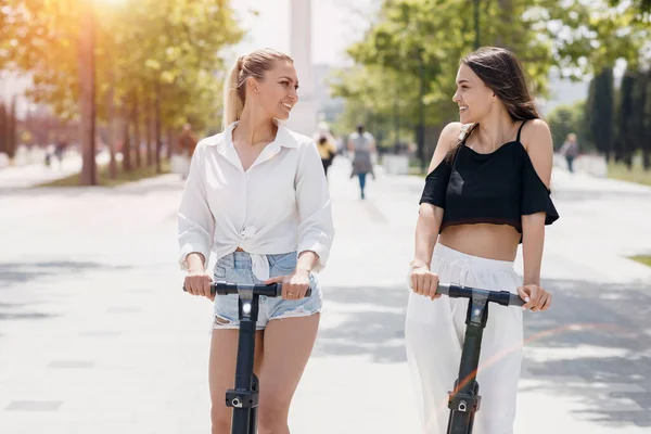 Duas mulheres amigas montando scooters elétricos no parque — Fotografia de Stock