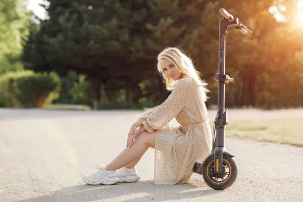 Mujer joven con scooter eléctrico al atardecer — Foto de Stock