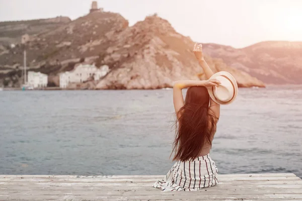 Back side young smiling happy woman sitting near sea on a pier — Stock Photo, Image