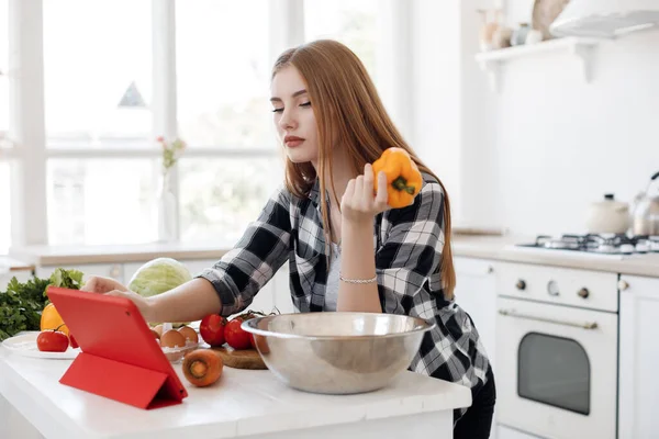 Young woman cooking at home at kitchen with tablet in ear plugs — Stock Photo, Image