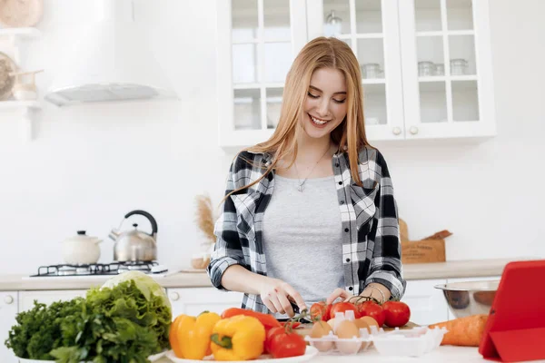 Молодая женщина готовит дома на кухне с планшетом — стоковое фото