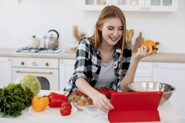 Young woman cooking at home at kitchen with tablet in ear plugs — Stock Photo, Image