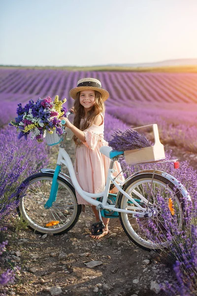 Pretty little girl with flowers and straw hat having fun in lavender field. Preteen girl with bicycle. — Stock Photo, Image