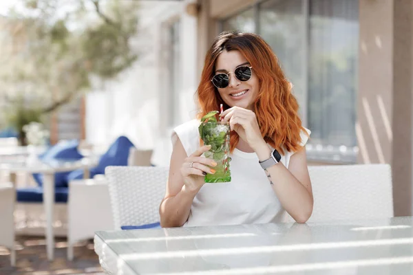 Schoonheid portret van glamour gember vrouw in zonnebril, het drinken van smakelijke koude cocktail, stad cafe terras, in de buurt van het strand — Stockfoto