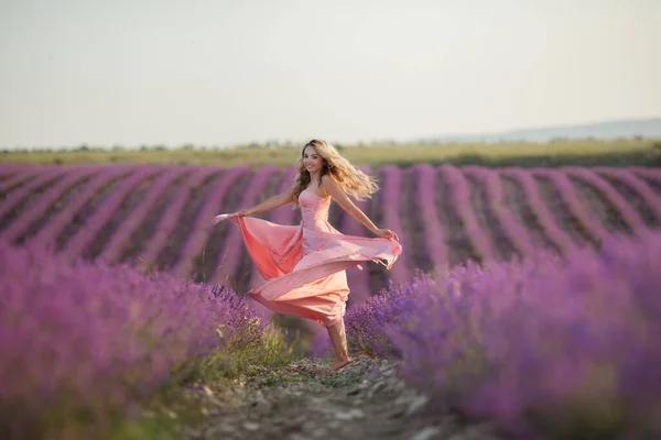 Pretty blonde woman running away in lavender field. woman in long dress and straw hat having fun in flowers of lavender — Stock Photo, Image