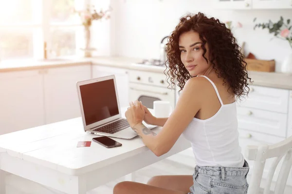 Evde dizüstü bilgisayarla çalışan kıvırcık saçlı genç bir kadın. — Stok fotoğraf