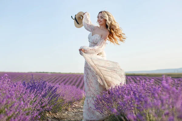 Hübsche blonde Frau auf der Flucht in Lavendelfeld. Frau in langem Kleid und Strohhut amüsiert sich in Lavendelblüten — Stockfoto