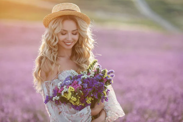 Pretty blonde woman running away in lavender field. woman in long dress and straw hat having fun in flowers of lavender — Stock Photo, Image