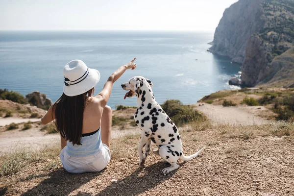 Parte trasera sentada mujer con un perro dálmata al aire libre cerca del mar azul — Foto de Stock
