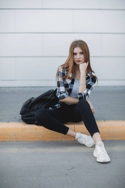 Gri arka planda oturan genç moda kadını.