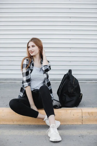 Giovane donna di moda seduta all'aperto vicino a sfondo grigio — Foto Stock
