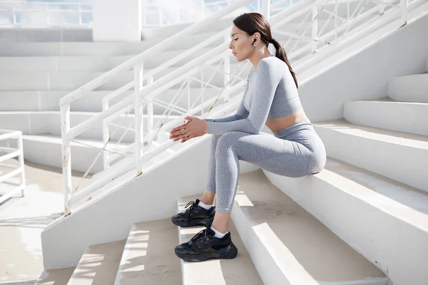 Retrato de fitness mujer al aire libre sentado en las escaleras en el estadio —  Fotos de Stock