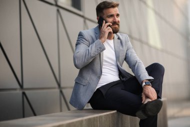 Dışarıda sakallı ve telefonlu bir adamın portresi.