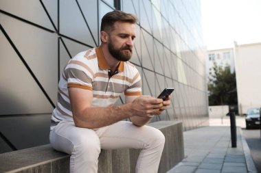 Dışarıda sakallı ve telefonlu bir adamın portresi.