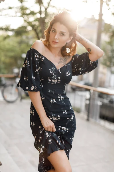 Heureuse jeune femme marchant dans la rue de la ville au coucher du soleil lumière chaude. Sourire fille émotionnelle en plein air en robe d'été — Photo