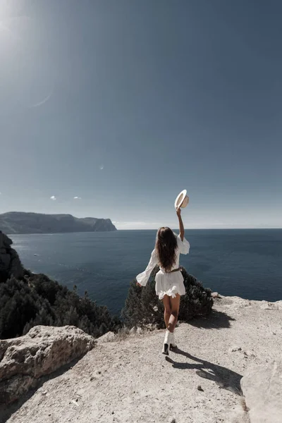 Parte de trás moda jovem mulher no vestido com chapéu ao ar livre perto do mar oceano — Fotografia de Stock