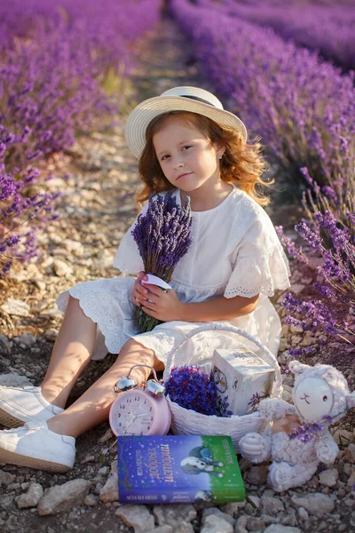 Een mooi meisje in een witte jurk en een hoed die plezier heeft in het bloeiende lavendelveld. portret in bloemen — Stockfoto