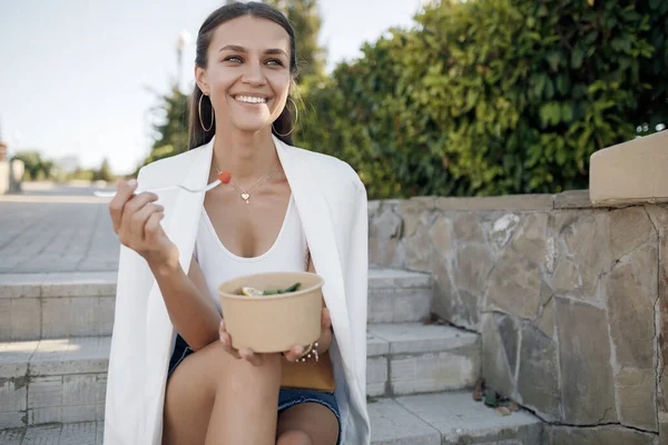 Boldog fiatal gyönyörű nő eszik friss ételt tálban az utcán — Stock Fotó