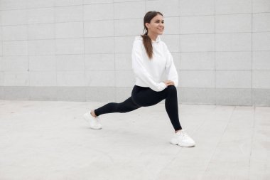 Açık havada esneme hareketleri yapan fit ve sportif genç bir kadının portresi.