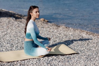 Kafkasyalı genç kadın deniz kıyısında yoga yapıyor.