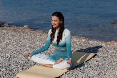 Kafkasyalı genç kadın deniz kıyısında yoga yapıyor.