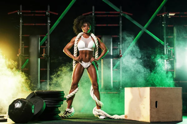 Mladá žena v tělocvičně s lanem bitva, v krásné sportovní, na tmavém pozadí se barva světla. — Stock fotografie