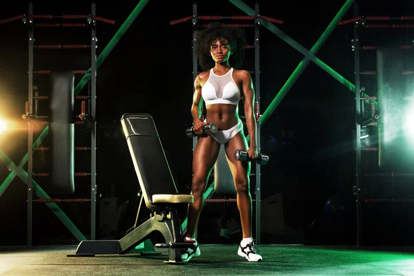 Mladá žena v tělocvičně se činka, v krásné sportovní, na tmavém pozadí se barva světla. — Stock fotografie