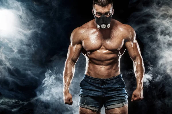 Muscular young fitness sports man in training mask. Workout with dumbbell in fitness gym. Copy space for fitness nutrition ads. — Stock Photo, Image