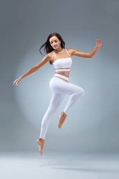 Vonzó izgatott fitness lány, balerina táncos sportruházat jumping az öröm, elszigetelt, felett szürke háttér. — Stock Fotó