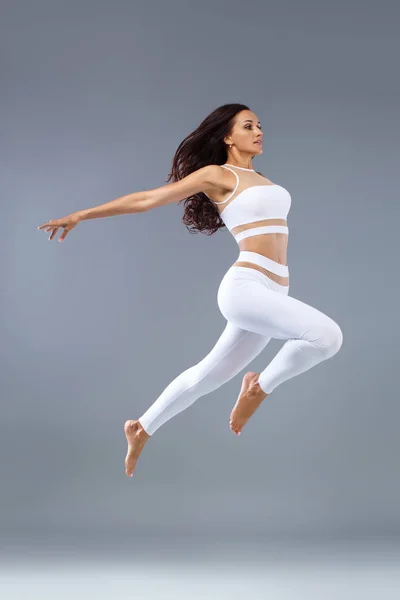 Atractiva chica fitness excitada, bailarina en ropa deportiva saltando de alegría aislada sobre fondo gris . —  Fotos de Stock