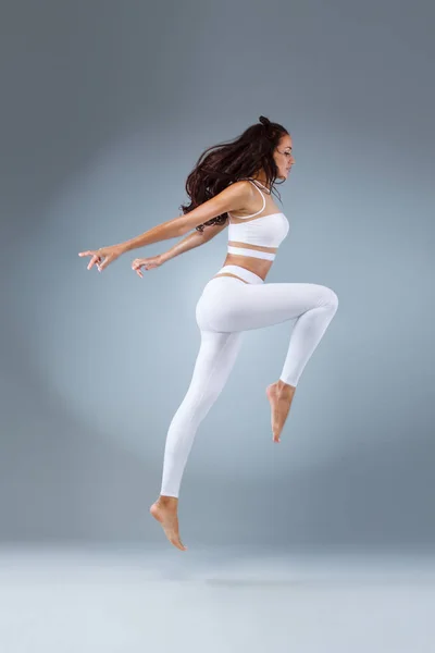 Vonzó izgatott fitness lány, balerina táncos sportruházat jumping az öröm, elszigetelt, felett szürke háttér. — Stock Fotó