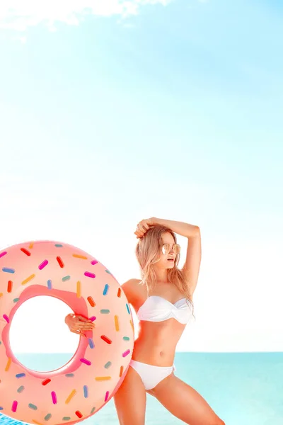 Vacaciones de verano. Disfrutando de una mujer bronceadora en bikini blanco con colchón de rosquillas cerca del océano . — Foto de Stock