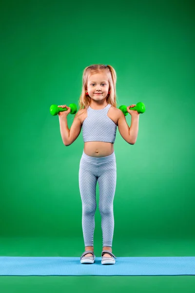 Дитяча дівчинка робить фітнес або вправи для йоги з гантелями ізольовані на зеленому фоні — стокове фото