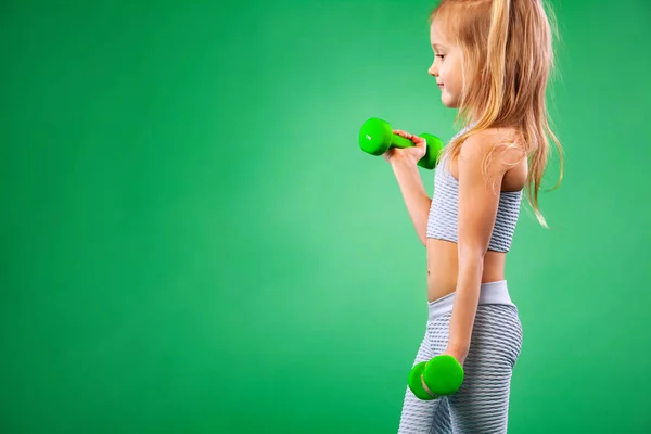 Дитяча дівчинка робить фітнес або вправи для йоги з гантелями ізольовані на зеленому фоні — стокове фото